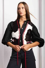 Chaleco de cuero con estampado de vaca en blanco y negro, con detalles de costuras rojas y botones de madera. La espalda es de lino negro con pasamanería de cuero.