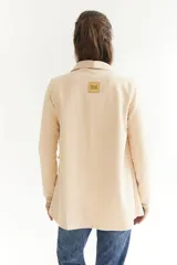 Blazer beige de tela agamuzada, corte recto y solapas clásicas.