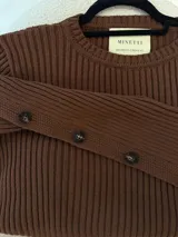 Sweater marrón de punto acanalado con cuello redondo y botones decorativos en las mangas.