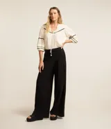 Blusa color crema de tricolina con detalles de ondas negras en cuello, mangas y frente. Tiene mangas 3/4 con volados y lazo en el cuello.