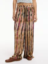 Pantalón de tiro alto con estampado tie-dye en tonos marrón, negro y rosa. Tiene pretina elástica ajustable con lazo, bolsillos laterales y corte palazzo.