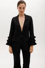 Blazer color beige confeccionado en lino, con cuello solapa, cierre frontal con un botón y mangas largas con volantes en capas.