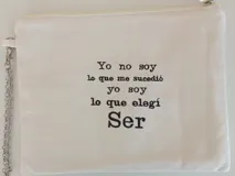 Sobre pequeño de tela color crema con cierre de cremallera y cadena metálica plateada. Estampado frontal con el dibujo de un ave fénix en color negro.