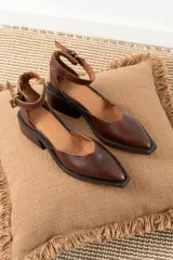 Zapato de cuero color marrón chocolate con punta cuadrada, corte lateral y pulsera al tobillo con hebilla dorada.