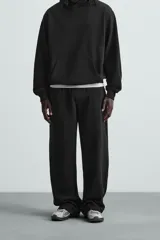 Pantalón jogger wide fit negro confeccionado en tejido de algodón con interior rizo. Pernera ancha, cintura elástica ajustable con cordón interior, bolsillos laterales y bolsillo trasero de plastrón.