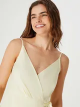 Vestido corto color amarillo pálido, con breteles finos, escote en V cruzado y lazo en la cintura.
