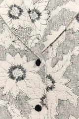 Blazer de tejido con estructura color crudo, con estampado de flores bordadas en negro. Tiene cuello solapa, manga larga y cierre frontal con botones negros.