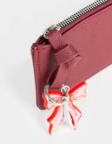 Monedero negro de cuerina con cierre circundante y charm colgante de moño rojo y torre Eiffel plateada.