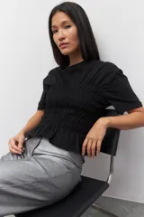Remera de algodón negra con fruncidos en la cintura y mangas cortas, diseñada con un corte ajustado.