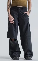 Pantalón negro con corte ancho, bolsillos laterales con solapa y detalle de cierre a la altura de la rodilla para convertirlo en short.