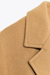 Abrigo largo color camel de Zara Woman Collection, confeccionado en hilatura con lana. Tiene cuello solapa con muescas, manga larga, falsos bolsillos delanteros, forro interior a contraste y cierre frontal con botones.