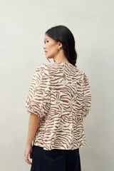 Blusa estampada color beige y blanco, con mangas abullonadas, escote redondo y lazos frontales.