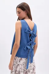 Musculosa de jean azul, sin mangas, con escote en V en la espalda que se cierra mediante dos lazos anudados.