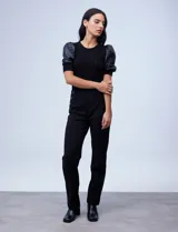 Pantalón negro de tiro alto y corte recto, confeccionado en tejido elastizado. Presenta un diseño frontal con botones decorativos aplicados en los laterales de la cintura y costuras verticales que estilizan la silueta.