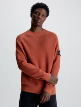 Sweater de punto texturizado color ladrillo, con cuello redondo, mangas largas raglán y logo de Calvin Klein en la manga.