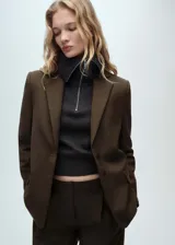 Blazer marrón oscuro de corte recto, con solapas de muesca, cierre frontal con botones, mangas largas con puños abotonados y dos bolsillos con solapa en la parte delantera.