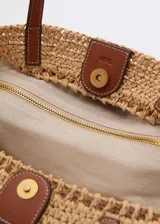 Bolso tipo shopper de fibra natural color beige, con doble asa de mano de cuero marrón y cierre regulable con botón magnético.