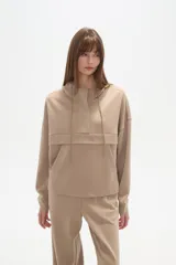 Buzo color beige con capucha, cordones ajustables, cuello alto y bolsillo canguro.