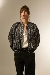 Campera estilo bomber de manga larga, con cuello mao y cierre frontal. Confeccionada en tejido de poliéster con estampado de piel de serpiente en tonos grises y negros.