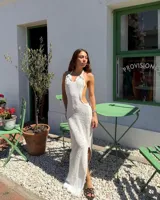 Vestido largo de tejido de punto blanco marfil, con escote halter anudado y aberturas pronunciadas en los laterales de la cintura. Presenta un tajo en la falda.