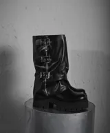 Bota de caña media de ecocuero color negro, con suela track, cierre lateral y tres hebillas decorativas con cierre de cremallera frontal.
