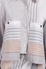 Camisa corta de algodón y seda con silueta recta, diseño a rayas verticales en tonos gris, blanco y beige, cuello camisero, cierre frontal con botones, mangas largas con puños abotonados, bolsillos de parche con botón a presión en el pecho y bajo recto.