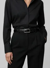 Cinturón fino de cuero sintético negro con textura de cocodrilo y hebilla rectangular metálica plateada.