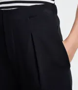 Pantalón zanahoria negro de punto roma, con cintura lisa, bolsillos laterales y pliegues delanteros.