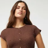 Camiseta marrón de punto gofrado con cuello redondo, mangas cortas y cierre frontal con botones dorados.