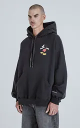 Buzo con capucha de calce oversize, color negro, con un pequeño estampado de Mickey Mouse en el pecho derecho. El cordón de ajuste de la capucha es negro con texto repetido en blanco.