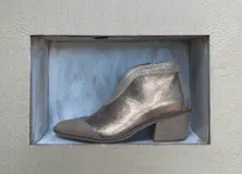 Botín de cuero color dorado con puntera y talón en gamuza color beige. Tiene cierre lateral y taco de madera.