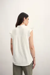 Camisa color amarillo pálido con cuello mao, sin mangas, con volados en los hombros y en el frente.