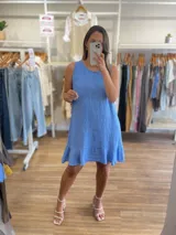 Vestido corto sin mangas, color beige claro, con cuello redondo y un volante o ruedo con volado en el bajo.