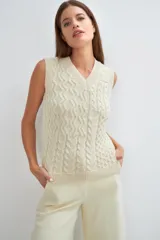 Chaleco tejido color crema con escote en v y sisas. Presenta un diseño con diferentes puntos combinados en el frente.