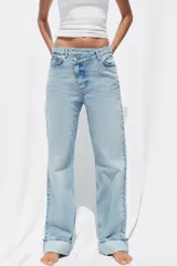 Pantalón de jean celeste de tiro alto, corte recto y largo hasta el tobillo con dobladillo. Tiene cinco bolsillos y cierre frontal cruzado con cremallera y botón.