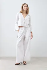 Pantalón de lino blanco de corte palazzo, con cintura elastizada y cordón ajustable. Presenta un vivo negro en el lateral.