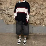 Chomba de manga larga negra con cuello polo blanco, franjas horizontales blancas y bordó, y detalles en blanco en los hombros.