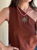 Collar corto con cuentas de nácar y dije de sol plateado hecho a mano en alpaca. Se cierra con cadena de acero quirúrgico y ganchito para regular el largo.