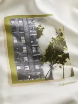 Buzo blanco de algodón con capucha y cordones ajustables. Estampado rectangular en el frente con fotografía de edificio y vegetación. Logo de Calvin Klein estampado debajo de la imagen.