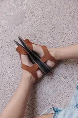 Sandalia plana de color tostado confeccionada en una combinación de neopreno y cuero. Posee un diseño de tira ancha con aberturas sobre el empeine, plantilla acolchada y suela de goma con costuras a la vista.