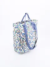 Mochila con estampado de dinosaurios y palmeras sobre fondo blanco, con asas de tela azul.
