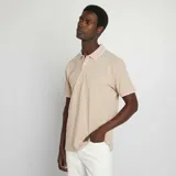 Remera polo color beige de piqué de algodón, con cuello clásico con borde blanco, tapeta de dos botones y mangas cortas con borde blanco.