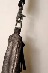 Bolso bandolera de cuero color marrón oscuro con acabado metálico, forro de algodón y herrajes plateados. Tiene correa ajustable y removible, cierre superior y bolsillo frontal con cremallera.