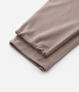 Pantalón baggy color beige, confeccionado en algodón con felpa. Presenta cintura elástica con cordón ajustable, bolsillos delanteros y un bolsillo trasero. El bajo es ajustable con elástico.