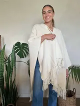 Ruana color crudo tejida a mano en punto arroz con lana merino. Presenta flecos en el borde inferior.
