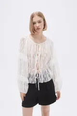 Blusa blanca traslúcida de encaje con mangas largas abullonadas y volados.