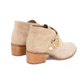 Bota corta de gamuza color avena, con diseño tipo botín chukka o desert boot modificado, que presenta una tira ancha cruzada sobre el empeine asegurada con una hebilla dorada. Posee taco bajo de madera.