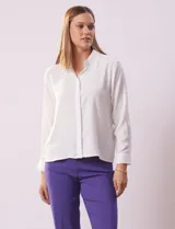 Camisa blanca de gasa, marca Sioni, con cuello con solapa, abertura central con botones y mangas largas con puño y botón.