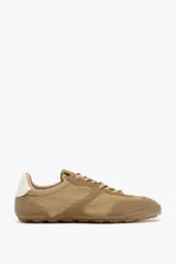 Zapatillas deportivas color beige con detalles en gamuza, estilo running, con suela dentada y ajuste con cordones.