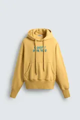 Sudadera con capucha color ocre, de corte holgado y mangas largas. Estampado frontal con texto en azul.